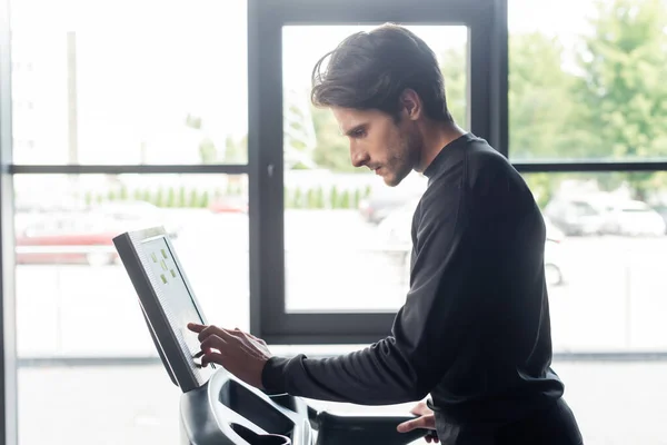 Side view of sportsman tuning treadmill while training in gym — Stock Photo