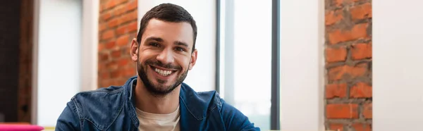 Молодий бородатий чоловік посміхається на камеру в кафе, банер — стокове фото
