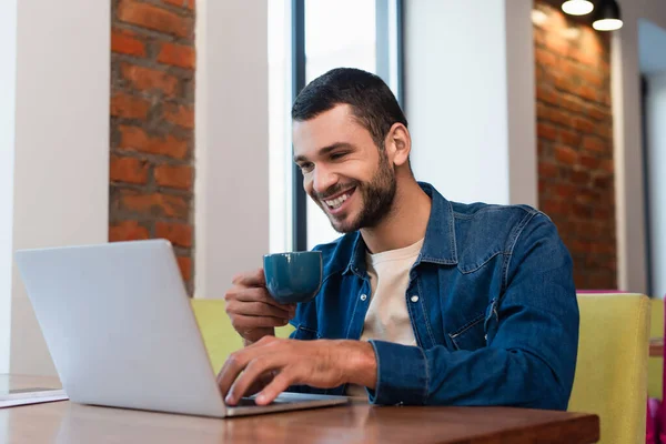 Hombre alegre escribiendo en el ordenador portátil mientras bebe café en el restaurante - foto de stock