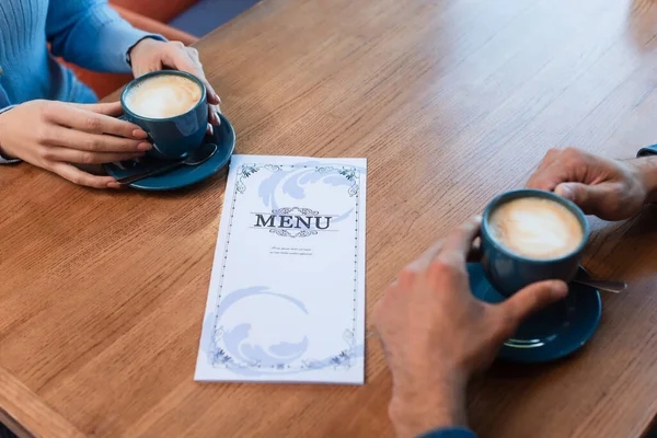 Vista parcial de pareja cerca de tazas de café y menú en la mesa - foto de stock