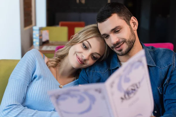 Happy couple sitting head to head while choosing meal from blurred menu — Stock Photo