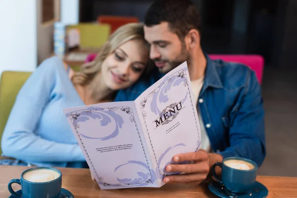 Casal borrado segurando menu perto de xícaras de café no restaurante — Fotografia de Stock