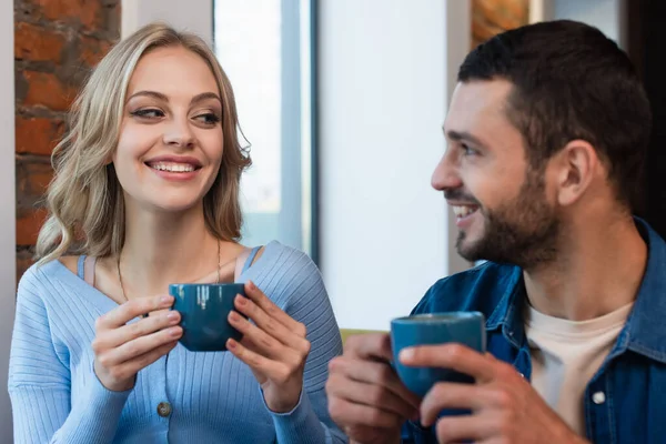 Happy woman looking at blurred man while drinking coffee in restaurant — Stock Photo