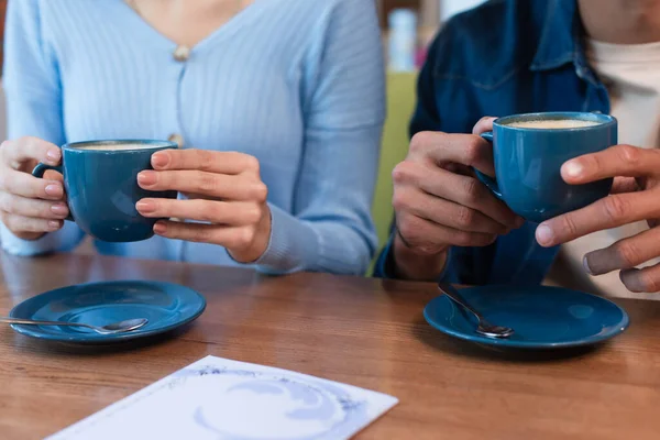 Cropped view of blurred couple holding coffee cups near menu on restaurant table — Stockfoto