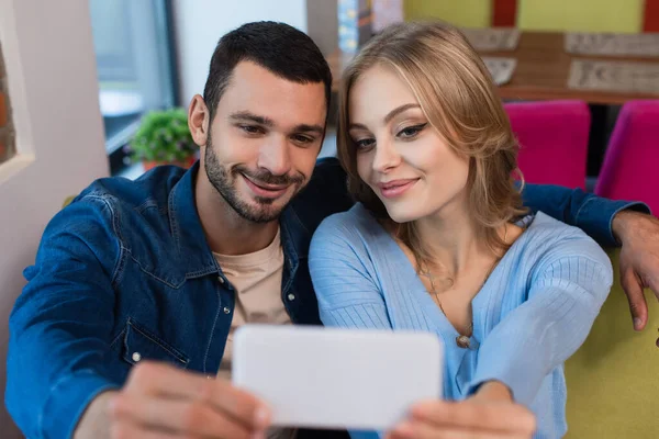 Casal satisfeito tomando selfie no celular desfocado enquanto passa o tempo no café — Fotografia de Stock