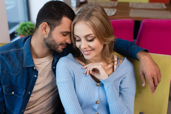 Happy man with closed eyes sitting near smiling blonde woman during romantic date in cafe — Foto stock