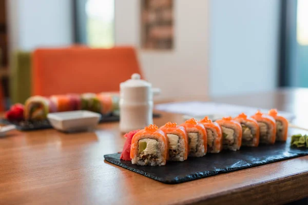 Enfoque selectivo de plato con rollos de sushi cerca de olla de salsa de soja y tazón sobre fondo borroso - foto de stock