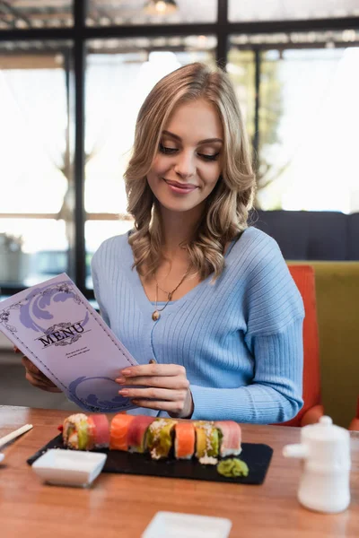 Femme souriante tenant menu près de délicieux sushis sur la table — Photo de stock