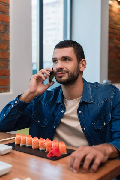 Smiling man talking on mobile phone near plate with sushi in restaurant — Fotografia de Stock