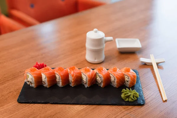Deliciosos rollos de sushi con caviar rojo cerca de la olla de salsa de soja y palillos en la mesa de madera - foto de stock