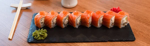 Black plate with tasty sushi rolls near chopsticks on wooden table, banner — Fotografia de Stock
