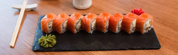 Черная тарелка с вкусными булочками суши возле палочек для еды на деревянном столе, баннер — стоковое фото