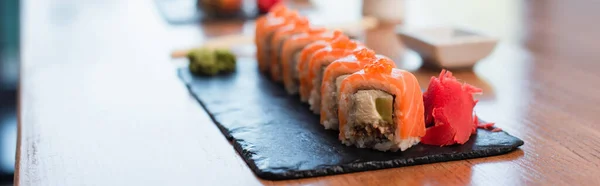 Vista de perto da placa preta com deliciosos rolos de sushi no fundo borrado, banner — Fotografia de Stock
