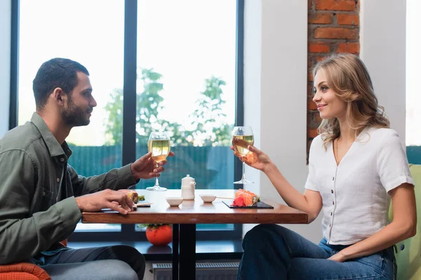 Side view of happy young couple holding glasses of white wine during dinner in sushi bar — Fotografia de Stock