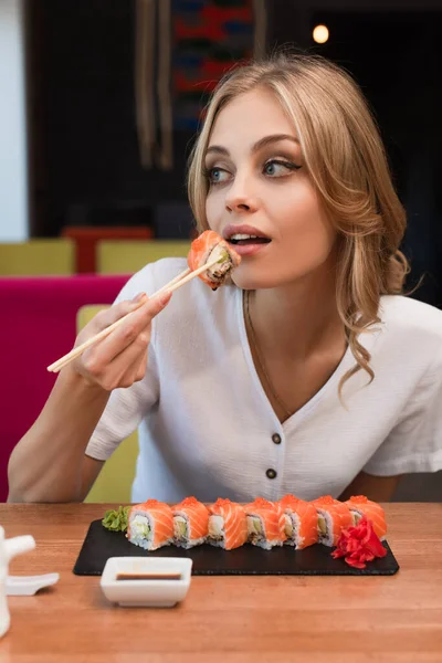 Jeune femme blonde manger de délicieux rouleaux dans le bar à sushi — Photo de stock