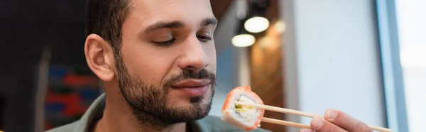 Young man with chopsticks holding delicious sushi roll, banner — Foto stock