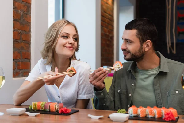 Pleased couple looking at each other while eating delicious sushi in restaurant — Foto stock