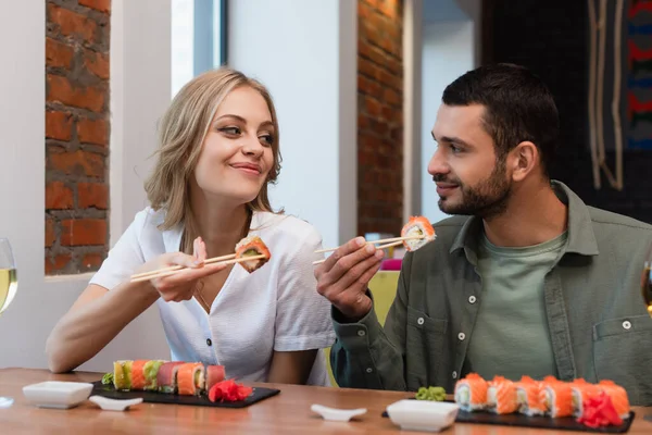 Pleased couple looking at each other while eating delicious sushi in restaurant — Stockfoto