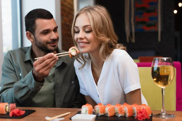 Young man feeding happy woman with sushi roll during dinner in restaurant — Stock Photo