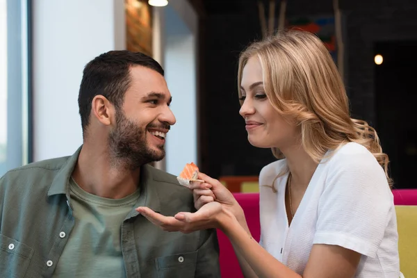 Alegre mujer alimentación novio con sushi roll durante romántico fecha en restaurante - foto de stock