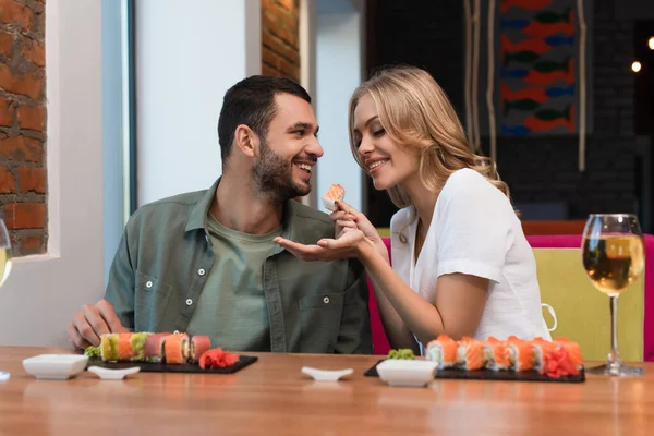 Cheerful woman feeding boyfriend with delicious sushi during date in restaurant — Stockfoto