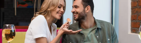 Happy woman feeding man with sushi roll during dinner in restaurant, banner — Stock Photo