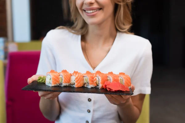 Vue recadrée de femme souriante avec assiette de délicieux rouleaux de sushi — Photo de stock