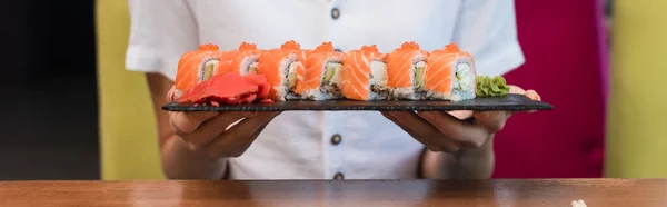 Visão parcial da mulher segurando placa com rolos de sushi saborosos, banner — Fotografia de Stock