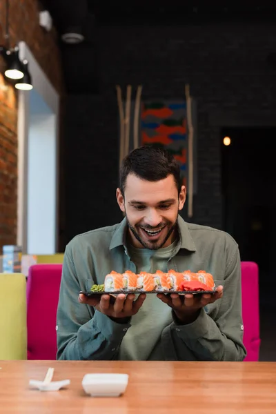 Homem espantado segurando prato com conjunto de deliciosos rolos de sushi no restaurante — Fotografia de Stock