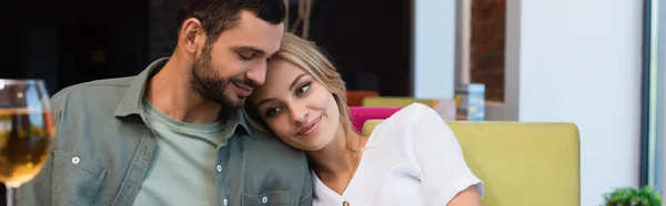 Happy woman leaning on shoulder of boyfriend near blurred glass of white wine, banner — Stock Photo
