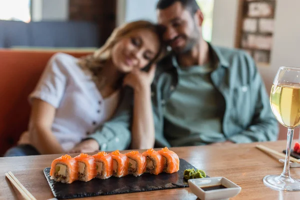 Selective focus of delicious sushi with red caviar and wasabi near blurred couple in restaurant — Fotografia de Stock