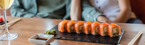 Vista cortada de casal desfocado perto do conjunto de sushi delicioso, tigela de molho de soja e copo de vinho branco, banner — Fotografia de Stock