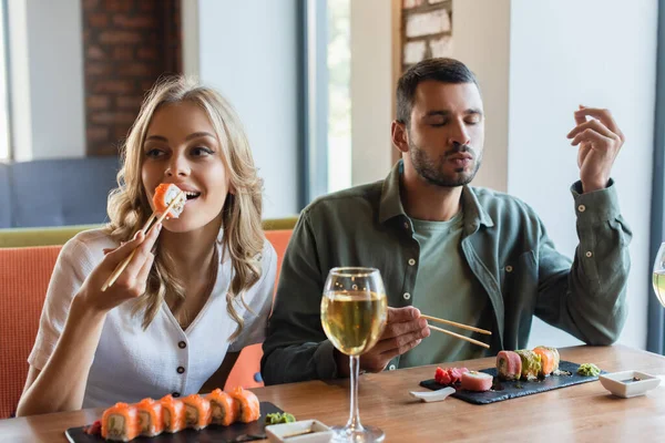 Man with closed eyes enjoying delicious sushi near smiling girlfriend — Stock Photo