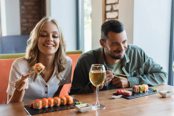 Fröhlicher Mann mit geschlossenen Augen isst Sushi neben lächelnder Freundin im Restaurant — Stockfoto