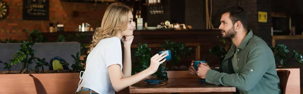 Vista laterale di una coppia felice che si guarda mentre tiene in mano tazze di caffè, banner — Foto stock