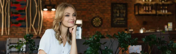 Молодая блондинка смотрит в сторону и улыбается в кафе, баннер — стоковое фото