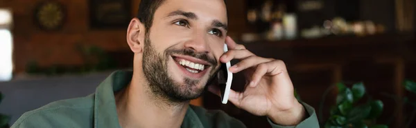 Hombre alegre hablando por teléfono móvil y mirando hacia otro lado en la cafetería, pancarta - foto de stock