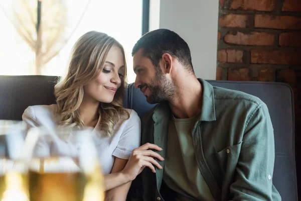 Young couple smiling during date in restaurant near wine glasses on blurred foreground — Stock Photo