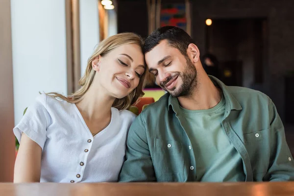 Heureux jeune couple avec les yeux fermés assis tête à tête dans le café — Photo de stock