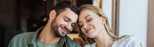 Young couple smiling with closed eyes while sitting head to head in cafe, banner — Fotografia de Stock