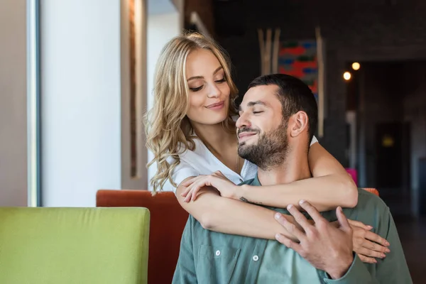 Young blonde woman embracing pleased boyfriend in restaurant — Stock Photo