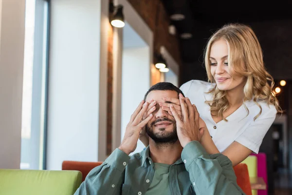 Mulher sorrindo cobrindo os olhos do namorado com as mãos enquanto joga adivinhar quem jogo — Fotografia de Stock