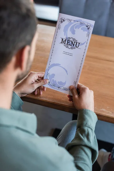 Vista recortada del hombre borroso celebración de menú en el restaurante - foto de stock