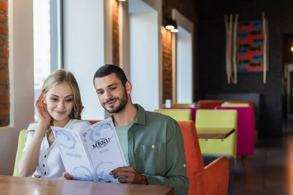 Улыбающаяся пара выбирает еду из меню, сидя в ресторане — стоковое фото