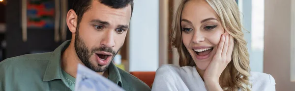 Pareja asombrada eligiendo la comida de menú borroso en el restaurante, pancarta - foto de stock