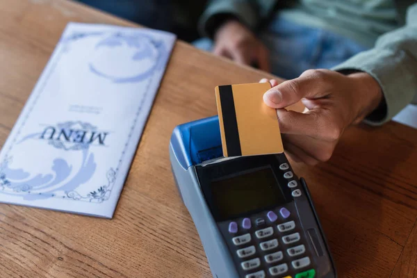 Vue partielle de l'homme avec carte de crédit près du terminal de paiement et brochure de menu sur la table — Photo de stock
