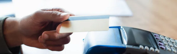 Cropped view of man holding credit card near payment terminal in cafe, banner — Stock Photo