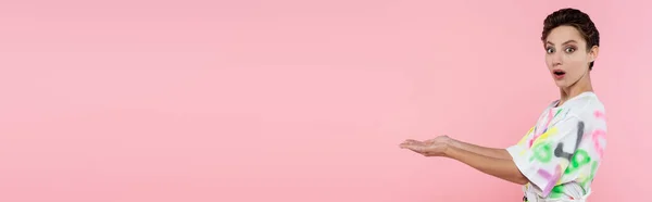 Amazed young woman pointing with hands while looking at camera isolated on pink, banner — Foto stock