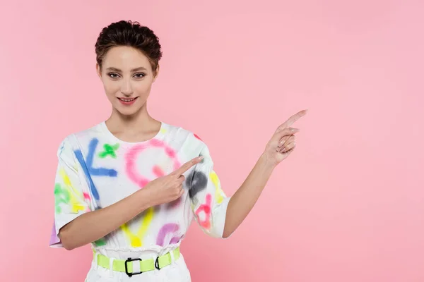 Trendige Frau lächelt in die Kamera und zeigt mit den Fingern auf rosa — Stockfoto