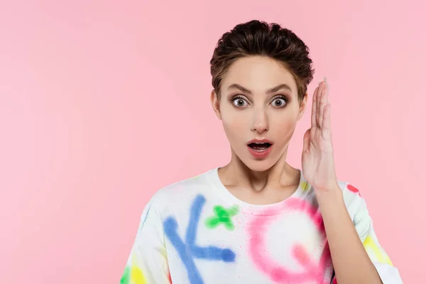 Mujer emocionada con la boca abierta sosteniendo la mano cerca de la cara mientras mira la cámara aislada en rosa - foto de stock